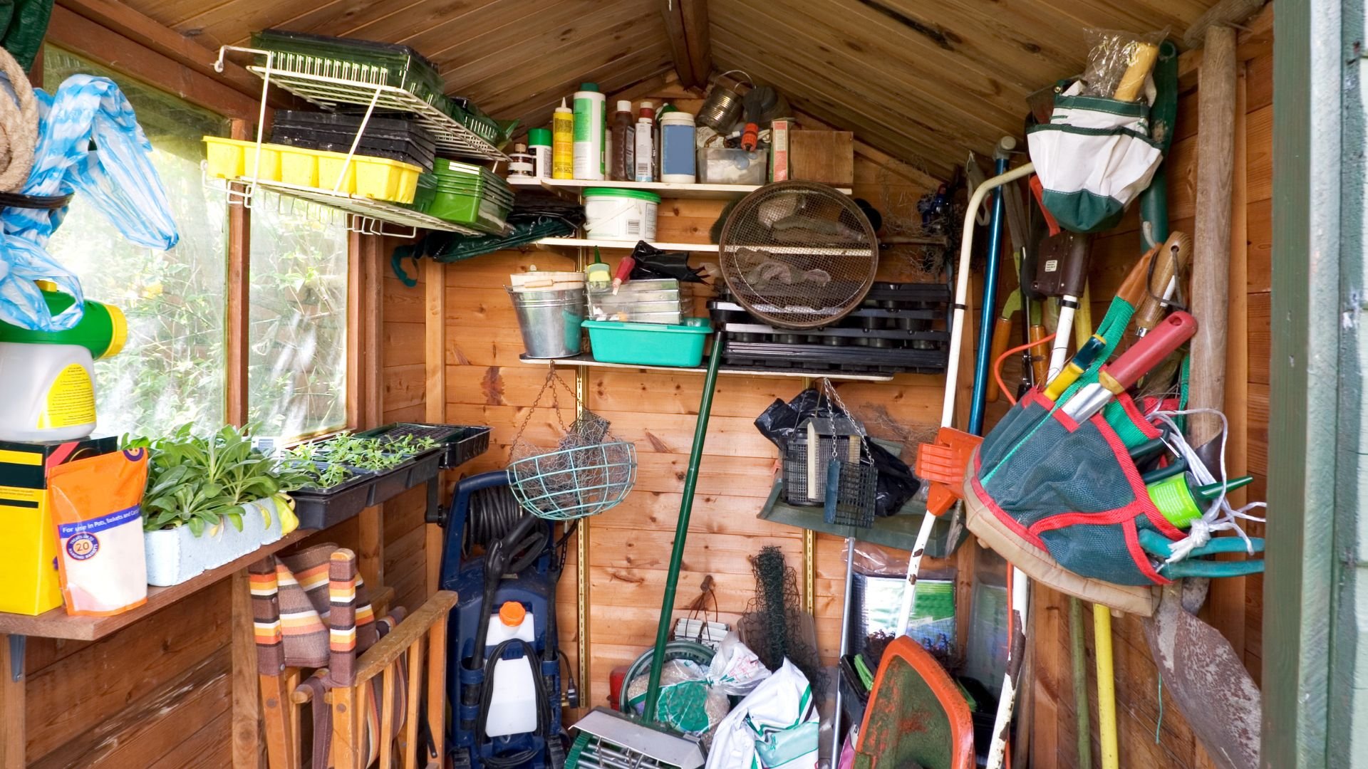 Cluttered garden shed with gardening tools, supplies, and seedling trays
