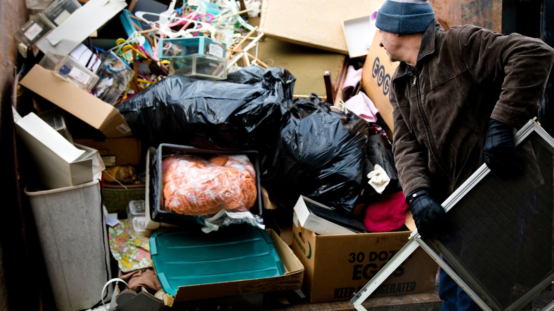 Person sorting through cluttered storage area with trash bags and boxes