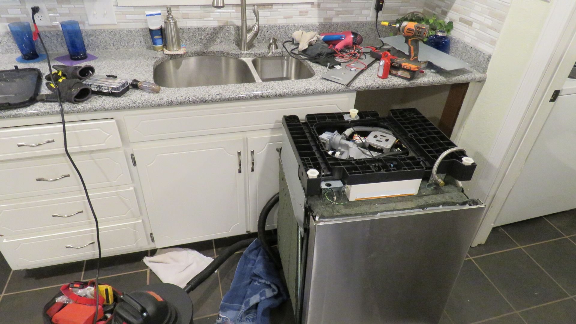 Cluttered kitchen counter with tools, sink, and disassembled appliance