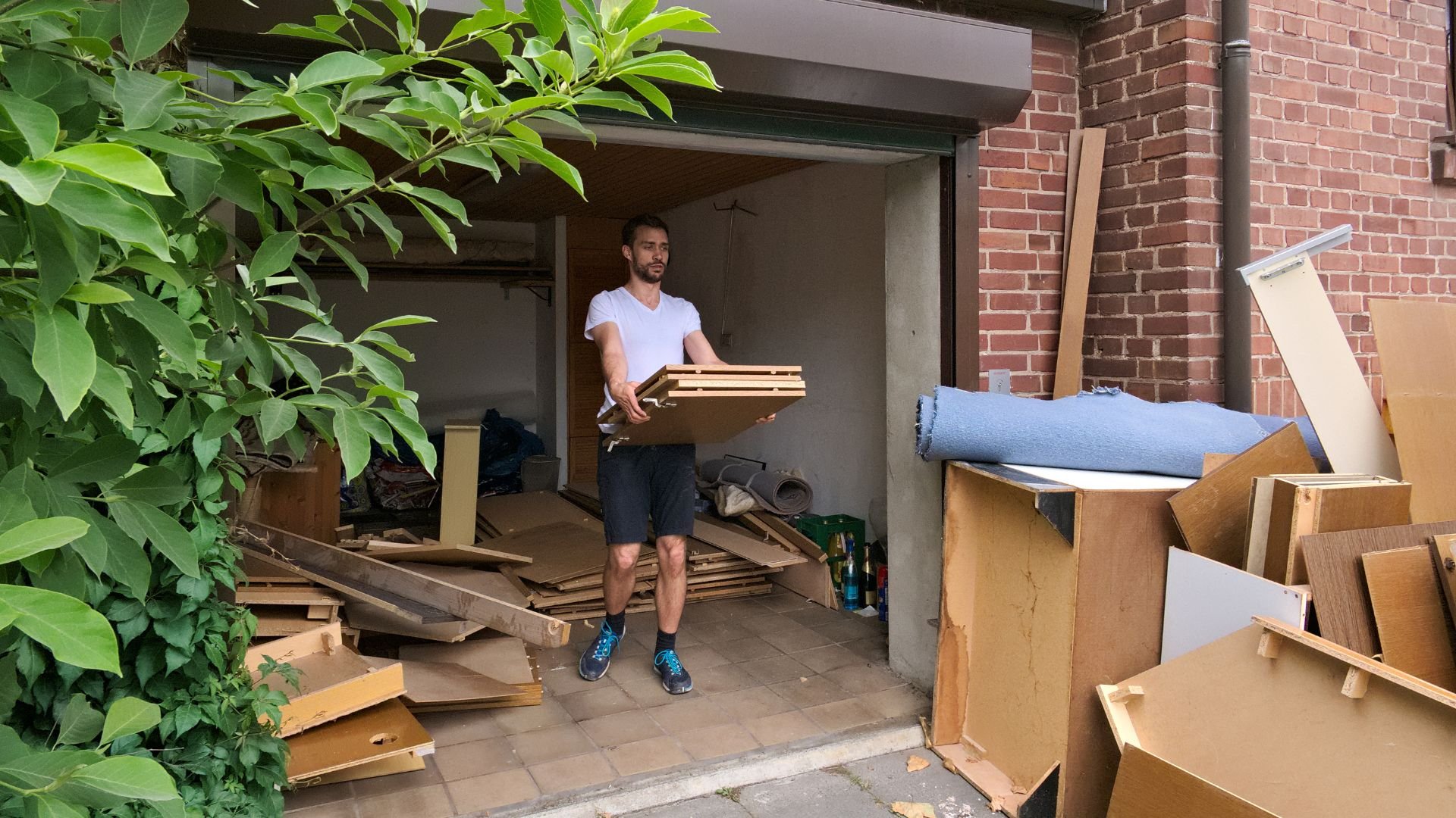 Person carrying wooden boards in cluttered storage area with cardboard boxes