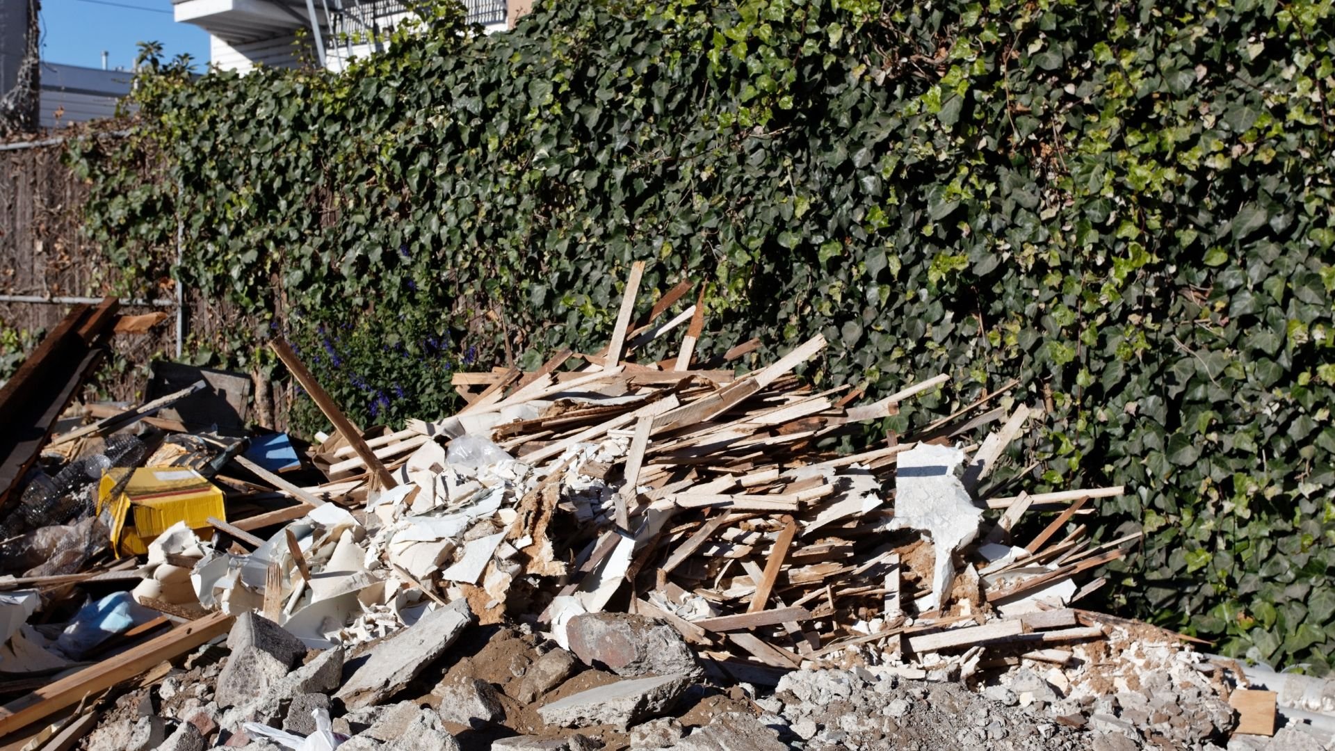 Pile of construction debris and wooden planks next to ivy-covered wall