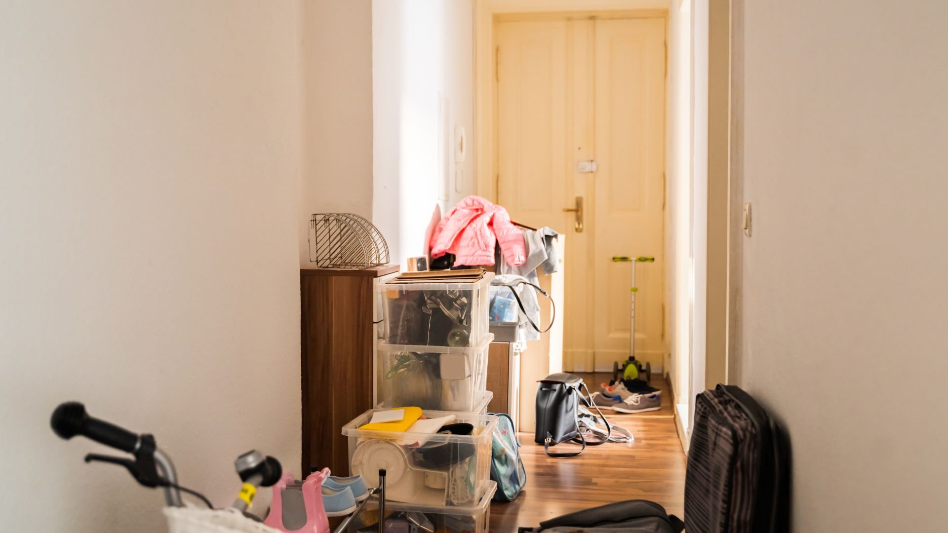 Cluttered entryway with clear storage boxes, shoes, and a bicycle handlebar