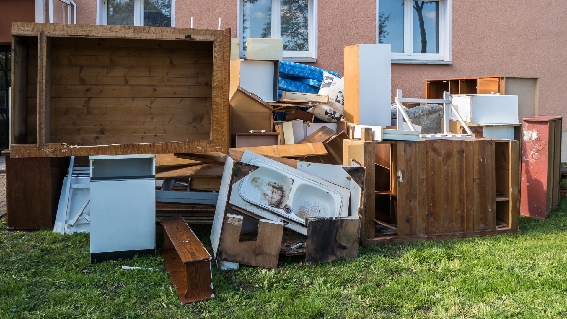 Pile of discarded wooden furniture and cabinets on grassy lawn